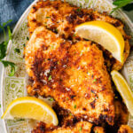 Parmesan crusted chicken breasts on decorative plate with lemon wedges and fresh parsley garnish, overhead view