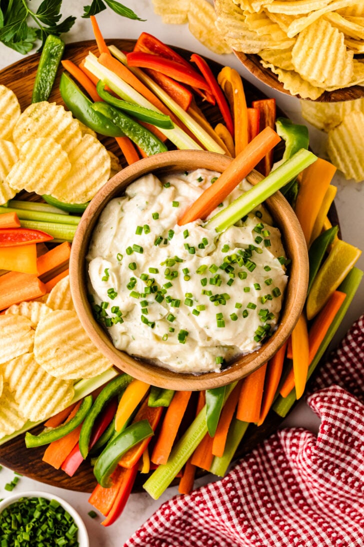 Whipped Ranch Dip in wooden bowl surrounded by colorful veggie sticks and wavy potato chips, topped with fresh chives, overhead view
