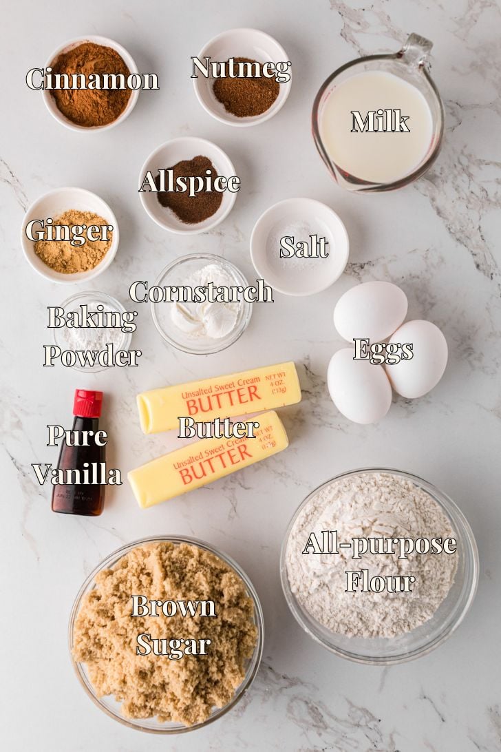 Ingredients for homemade spice cake arranged on a counter, including flour, brown sugar, butter, eggs, milk, and warm spices.