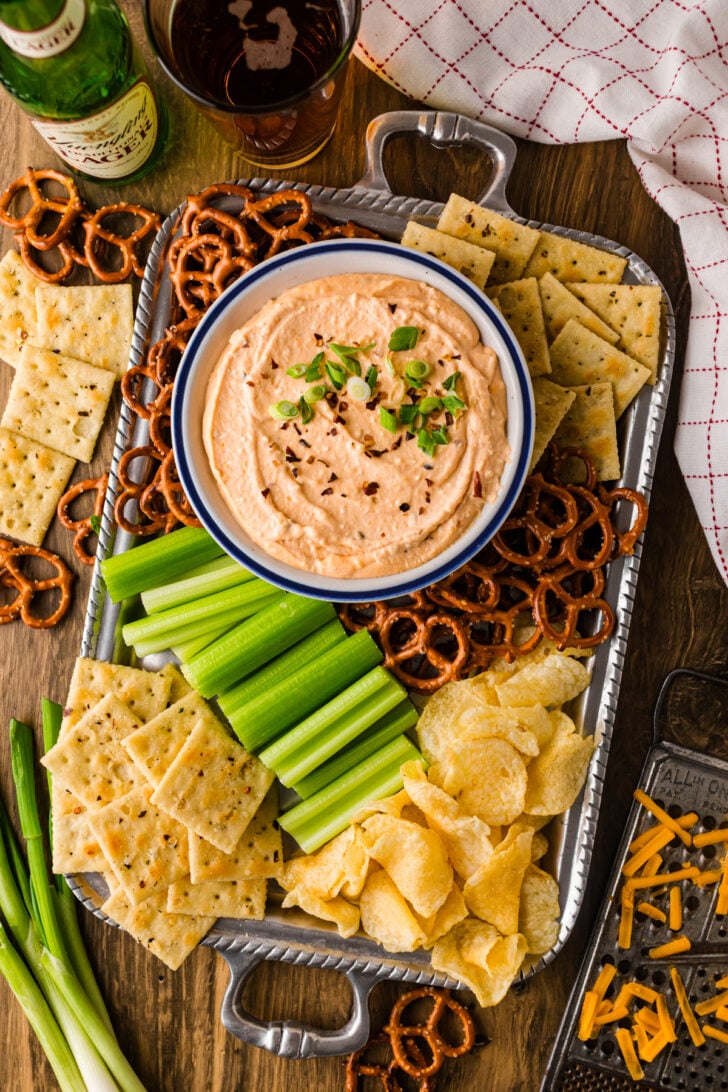 क्रॉक पॉट बियर चीज़ डिप का कटोरा, डिपर्स-प्रेट्ज़ेल, क्रैकर्स, और ब्रोकोली और गाजर जैसी ताजी सब्जियों के साथ।