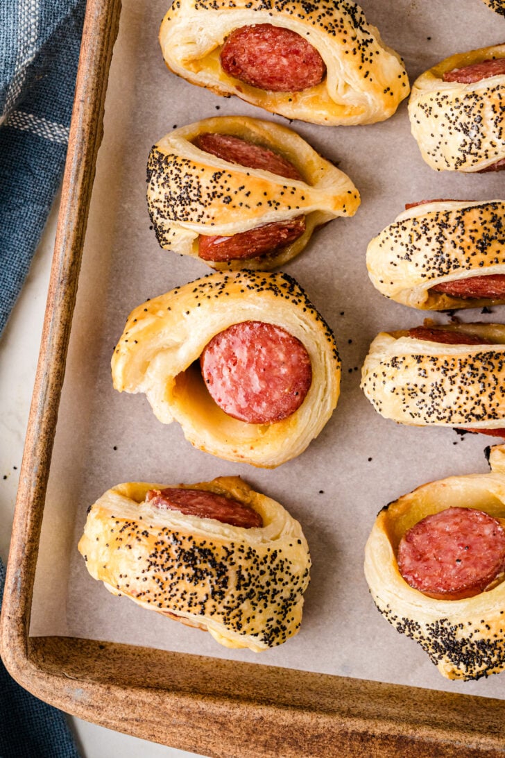 Baked puff pastry pigs in a blanket with smoked sausage, browned and flaky on a parchment-lined baking sheet.