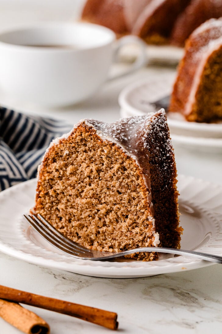 Slice of moist spice cake with vanilla glaze on a plate with a fork, showing the soft tender crumb inside.