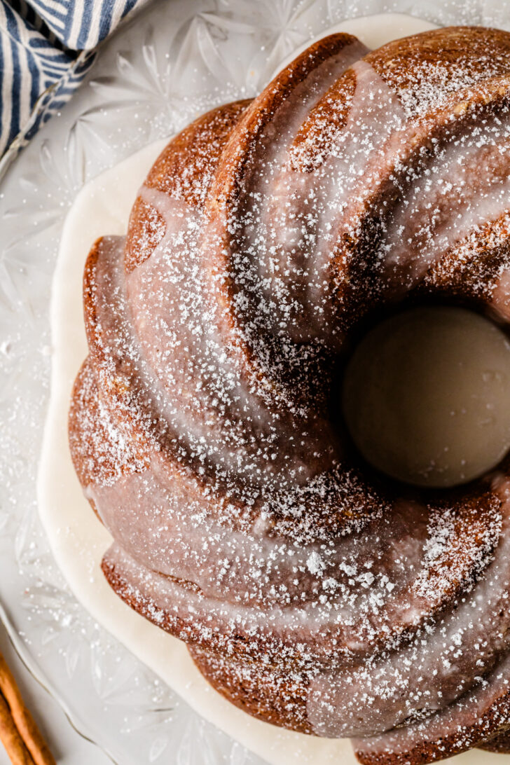 Moist homemade spice Bundt cake drizzled with vanilla glaze and dusted with powdered sugar on a cake stand.