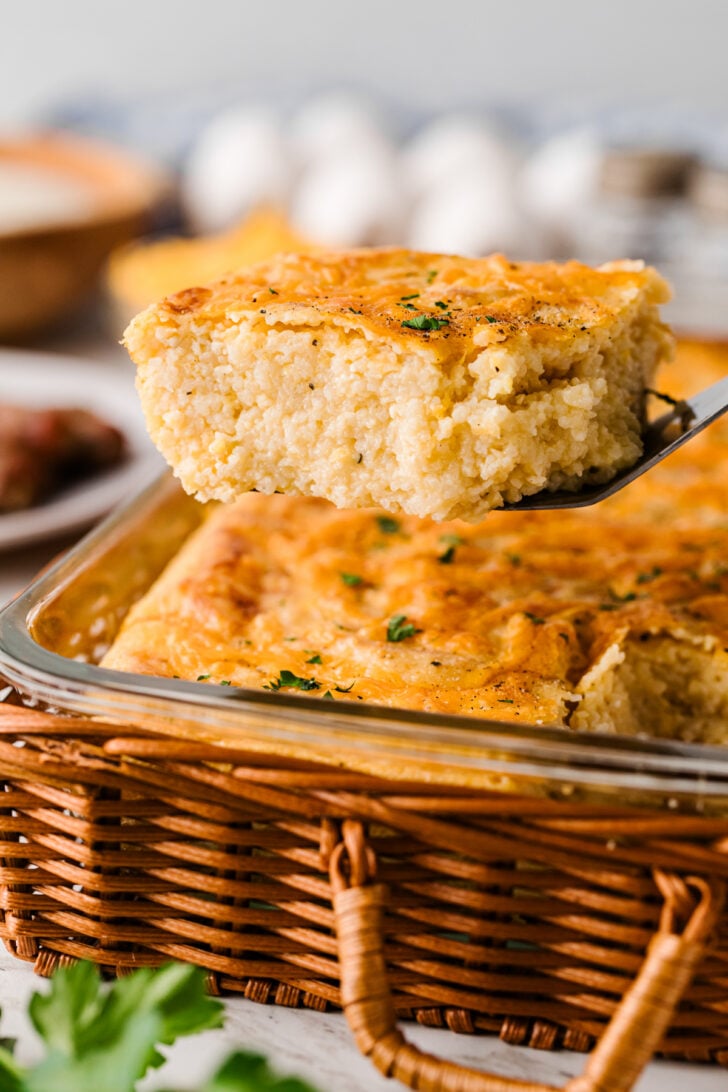 पके हुए पनीर के टुकड़ों को एक धातु के स्पैटुला पर उठाया गया है, जो इस दक्षिणी कैसरोल के अंदर मलाईदार और कुरकुरा सुनहरे किनारों को दिखाता है।