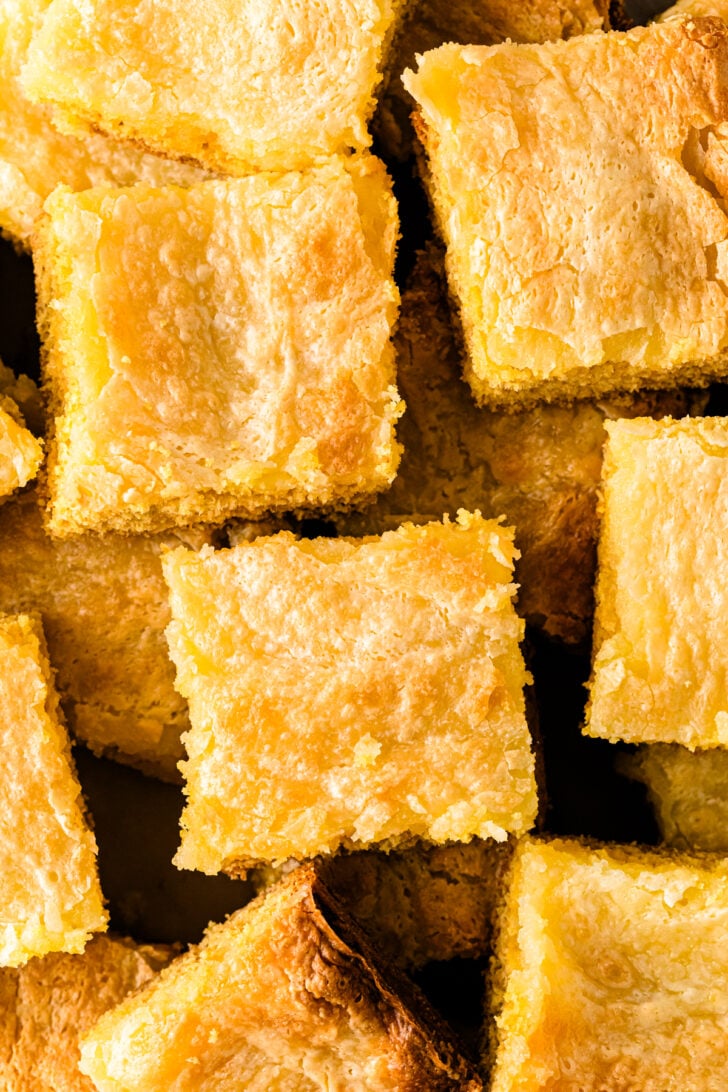 नीमन मार्कस केक के चौकोर टुकड़े पैन से काटे गए, जिसमें नरम पीला केक और गाढ़ा, कोमल टुकड़ा दिख रहा है।