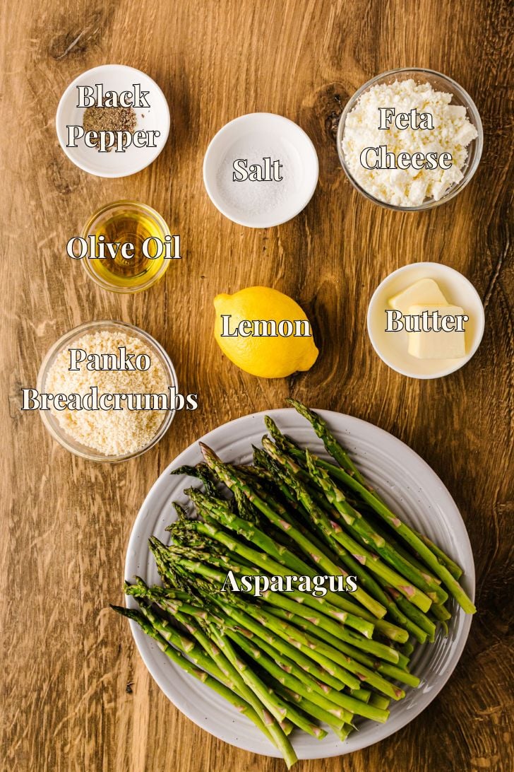 भुने हुए शतावरी रेसिपी के लिए ताजा शतावरी भाले, पैंको ब्रेडक्रंब, नींबू, फेटा और मक्खन को एक बोर्ड पर व्यवस्थित किया गया है।