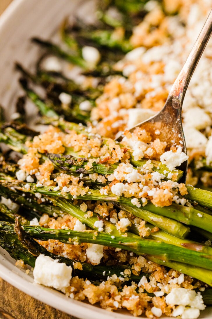 एक सर्विंग प्लेट पर नींबू पैंको और फेटा के साथ भुना हुआ शतावरी, आसान स्प्रिंग साइड डिश।