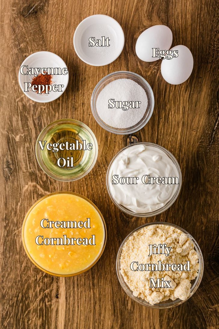 Jiffy corn muffin mix, sour cream, creamed corn, eggs, oil, sugar, and salt measured out on a white kitchen counter ready to make sour cream cornbread.