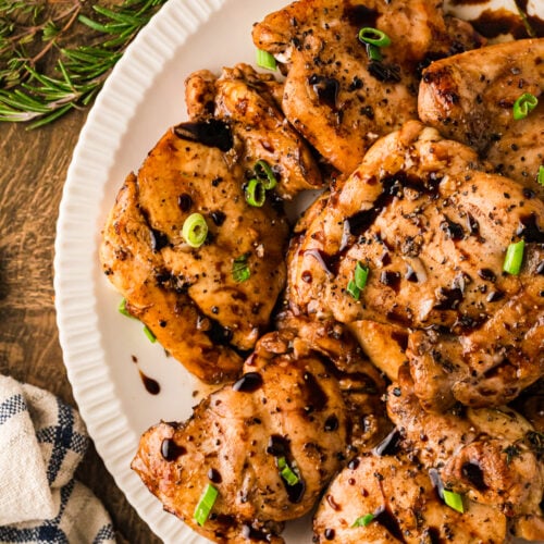 Balsamic chicken thighs 10 plated on white dish, topped with green onions and cracked pepper, overhead view on wooden table