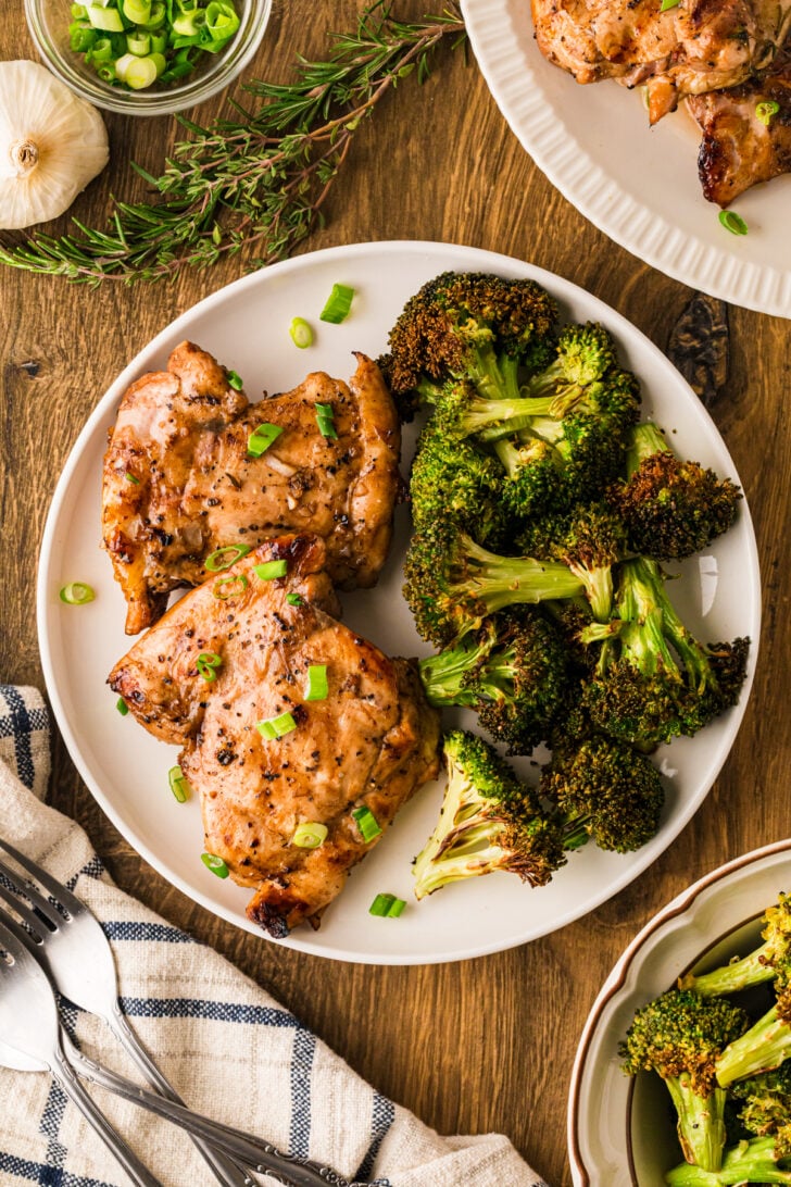 भुनी हुई ब्रोकोली के साथ एक सफेद प्लेट पर बाल्समिक ग्लेज़ चिकन जांघें, चमकदार बाल्समिक और हरे प्याज के साथ बूंदा बांदी।