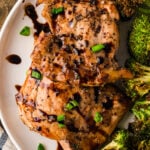 Balsamic chicken thighs glazed with green onions on white plate with roasted broccoli, overhead view