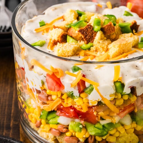 Southern Cornbread Salad layered in a glass bowl with cornbread crumbles, beans, corn, peppers, tomatoes, cheese, and creamy dressing topped