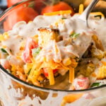 Southern Cornbread Salad served in a white speckled bowl with a spoon, topped with shredded cheese, tomatoes, and creamy dressing