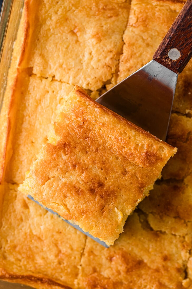 A thick slice of sour cream cornbread on a serving spatula showing the tender, moist golden crumb inside.