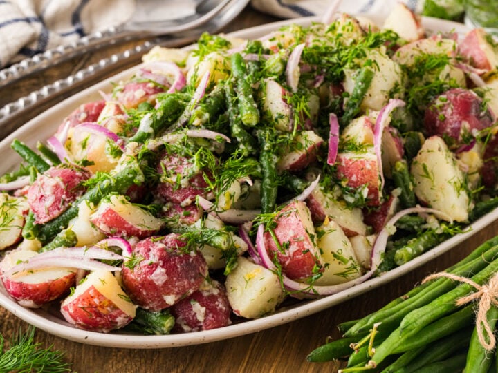 Green bean and potato salad on an oval platter with a bundle of fresh green beans.