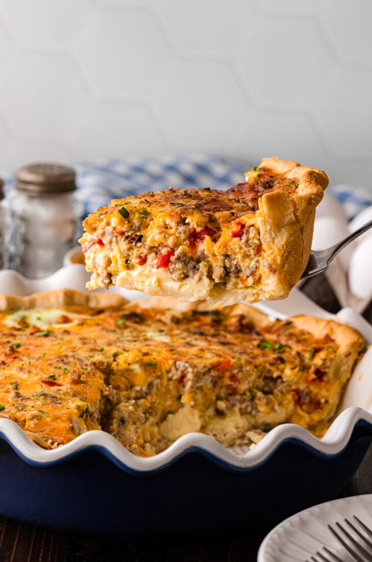 A golden slice of pimento cheese sausage quiche on a serving spatula, showing the creamy egg custard, savory sausage, and melted sharp cheddar filling inside a flaky deep dish crust.