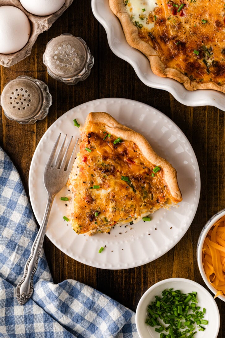 A close-up slice of pimento cheese sausage quiche garnished with fresh chopped chives, showing the rich, creamy custard and layers of sausage and melted cheddar inside a buttery golden crust.