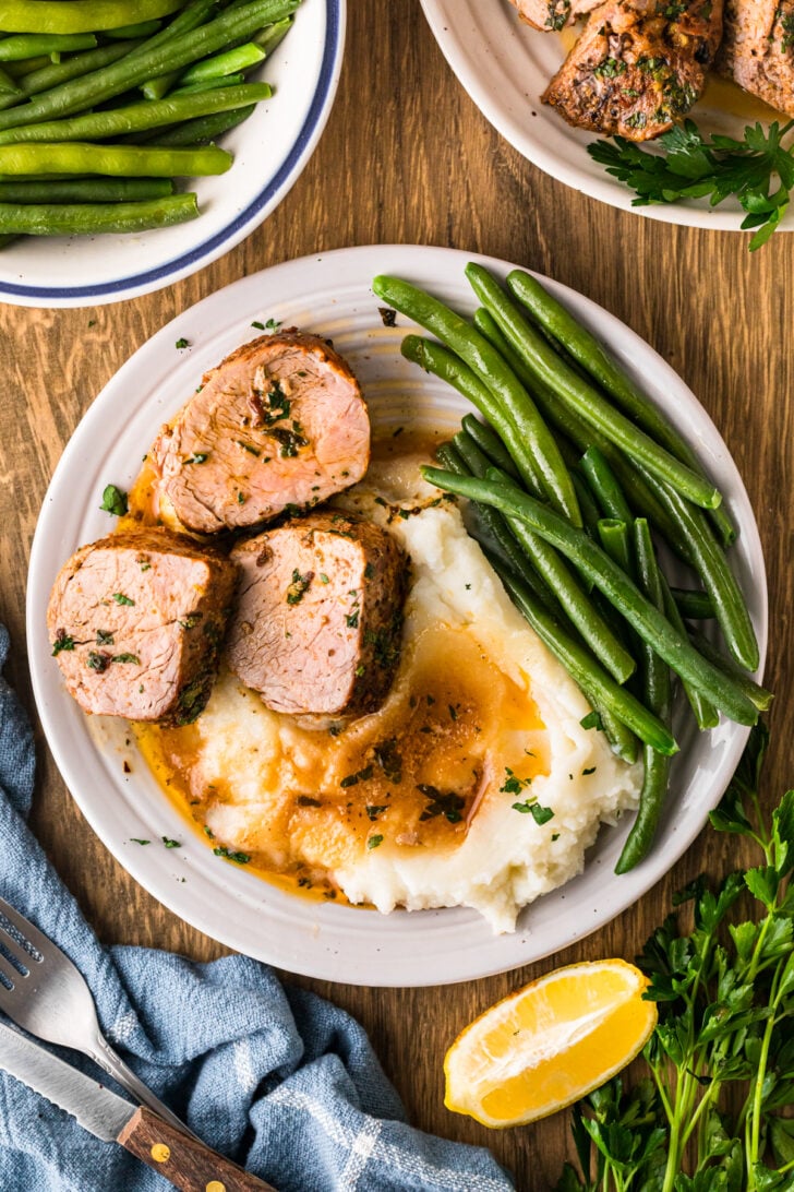 Sliced cast iron pork tenderloin on a dinner plate with creamy mashed potatoes and green beans.