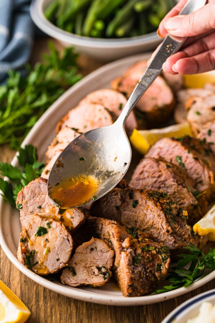 Spooning pan juices over sliced roasted pork tenderloin for a buttery herb finish.