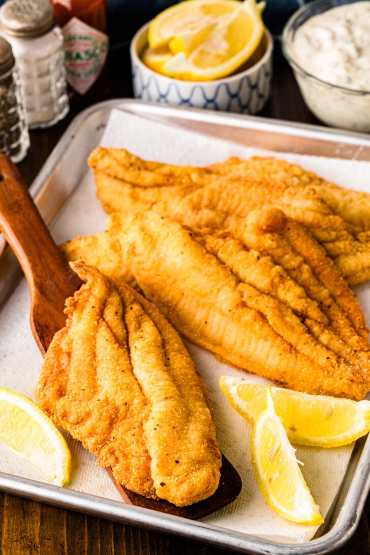 Crispy Southern fried catfish fillets served on a tray with lemon wedges and tartar sauce.