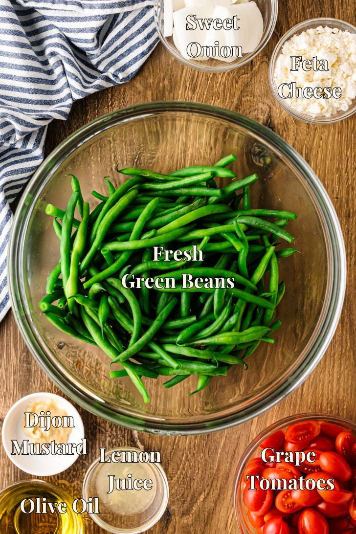 Ingredients for green bean salad, including fresh green beans, grape tomatoes, sweet onion, feta cheese, lemon juice, Dijon mustard, and olive oil.