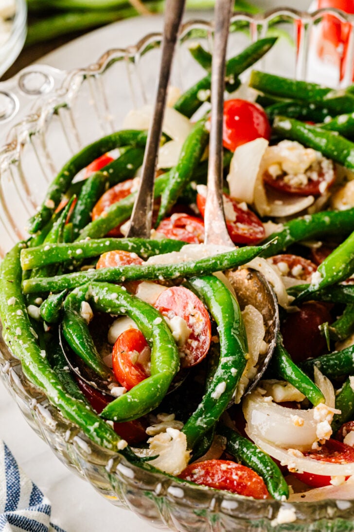 Green bean salad with tomatoes, onion, and feta being tossed in a bowl.