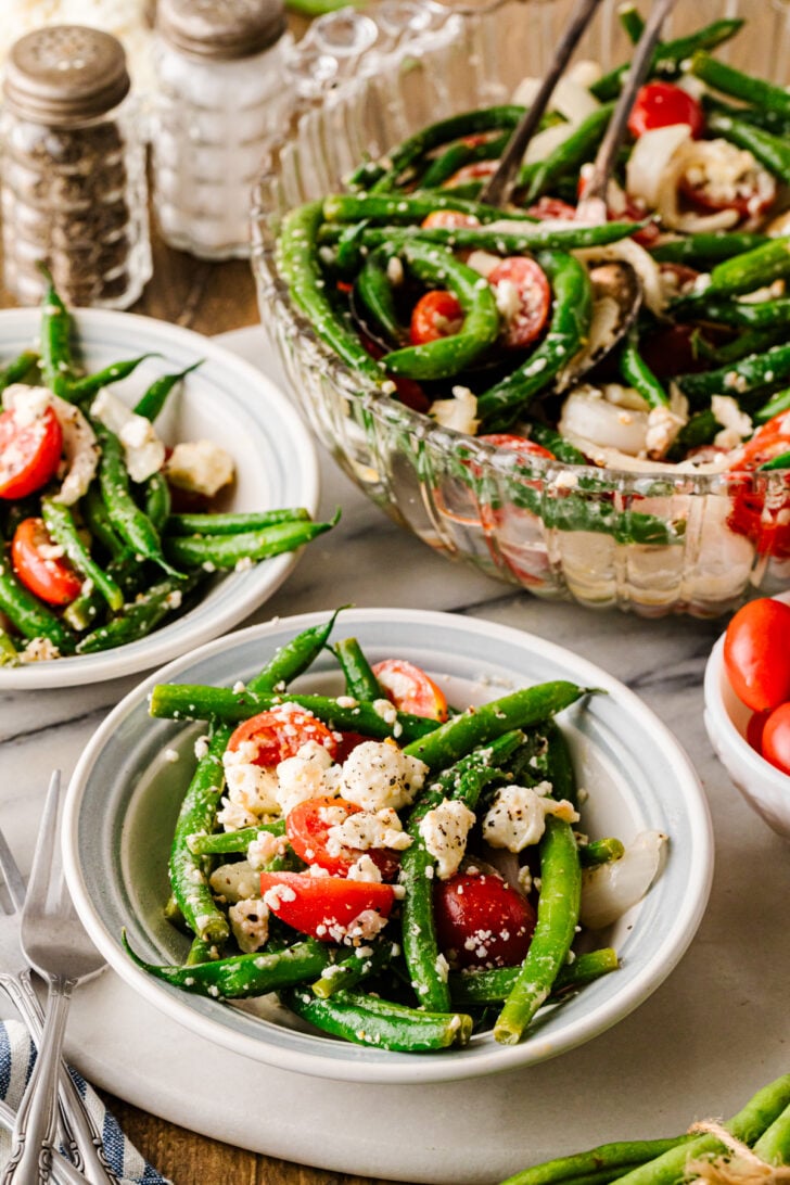 Green bean salad served in bowls with grape tomatoes, feta cheese, sweet onion, and herbs.