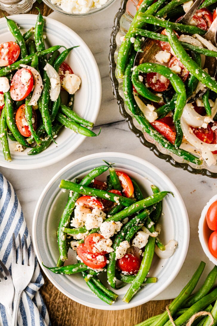 Fresh green bean salad with grape tomatoes, sweet onion, feta cheese, and herbs served in bowls.