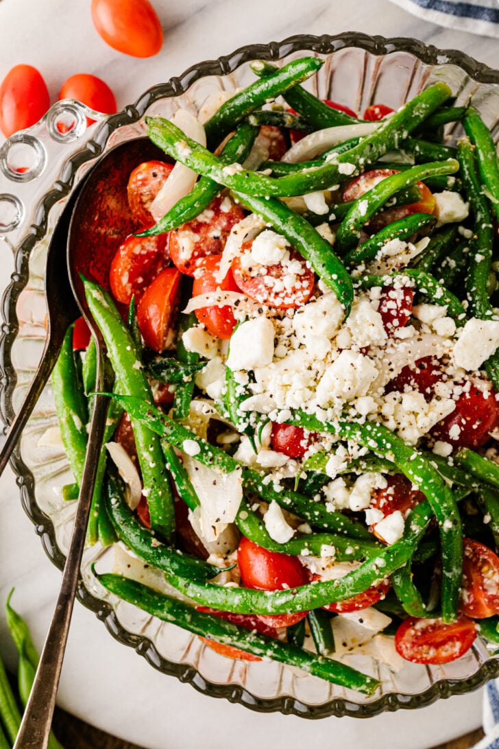 Finished green bean salad in a glass bowl with tomatoes, sweet onion, feta cheese, and herbs.