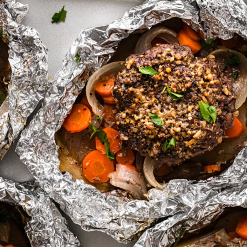 Hobo foil packs with burger patties, carrots, and onions, close-up view.