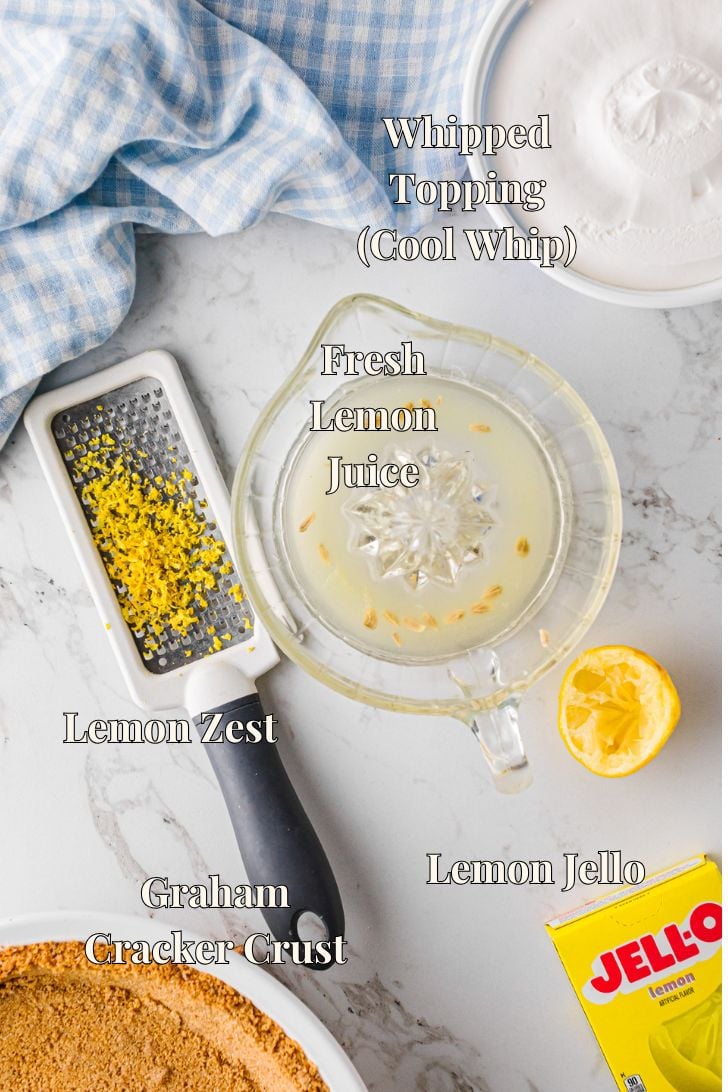 Lemon icebox pie ingredients including lemon Jello, Cool Whip, fresh lemons, and a graham cracker crust arranged on a white surface.