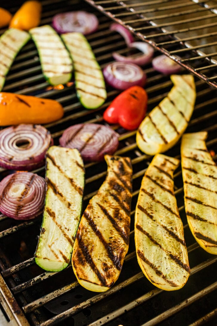Zucchini, onions, and peppers grilling on a barbecue.