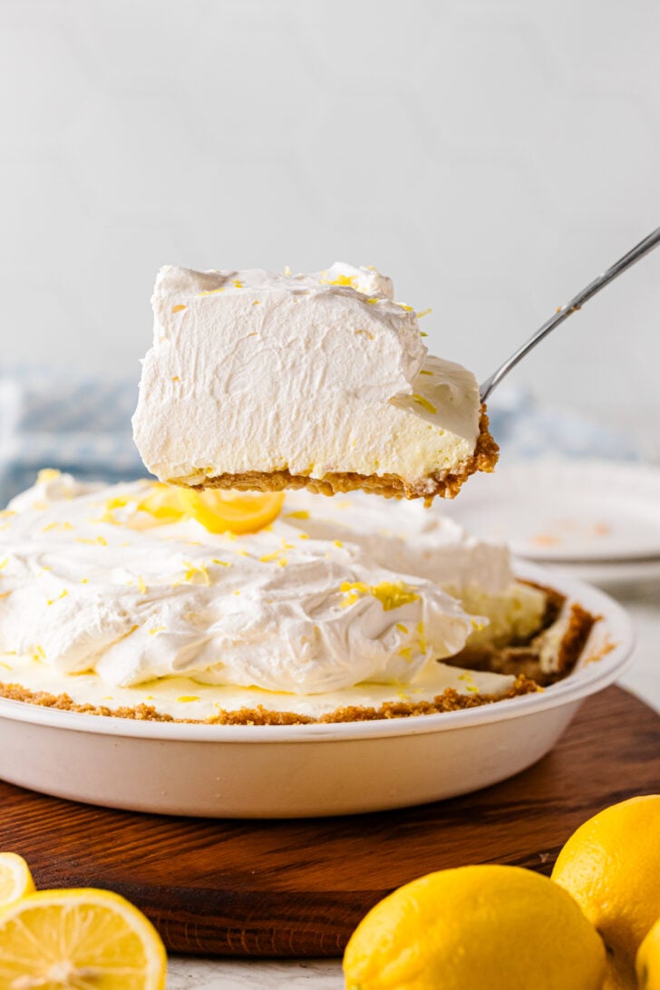 A slice of creamy no-bake lemon icebox pie lifted on a pie server showing the silky lemon filling and golden graham cracker crust.