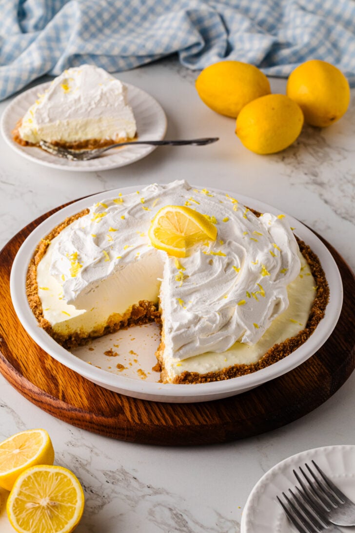 A slice of classic lemon icebox pie on a white plate with the whole pie on a white pie dish.