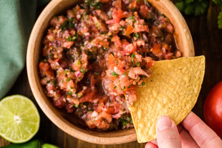 Tortilla chip scooping fresh homemade salsa from a wooden bowl