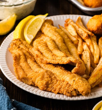 Plate of crispy fried catfish fillets with fries, hush puppies, lemon wedges, and tartar sauce