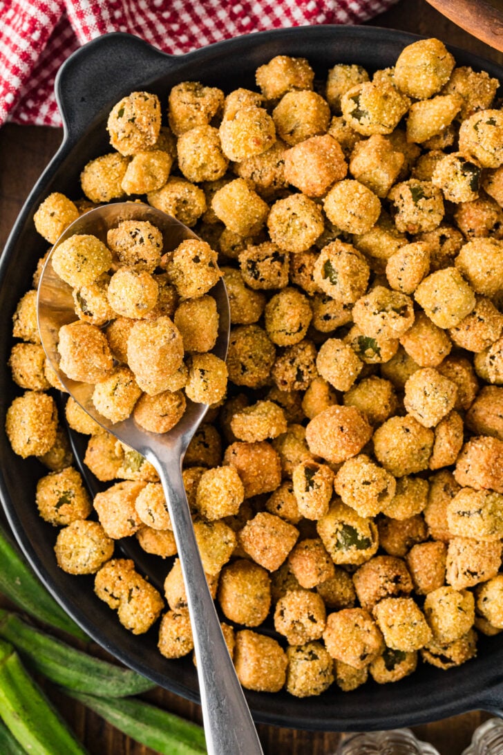 Fried okra scooped onto a spoon in a black skillet, overhead view.