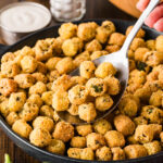 Hand scooping fried okra with a spoon from a black skillet.