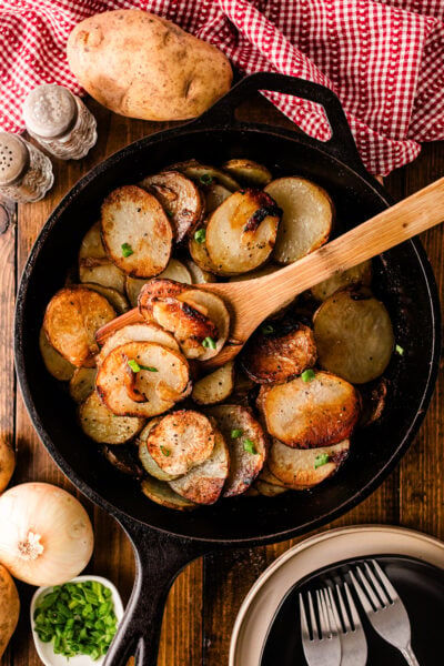 Southern fried potatoes and onions in a cast iron skillet with parsley and a wooden spoon
