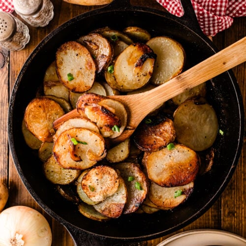 Southern fried potatoes and onions in a cast iron skillet with parsley and a wooden spoon