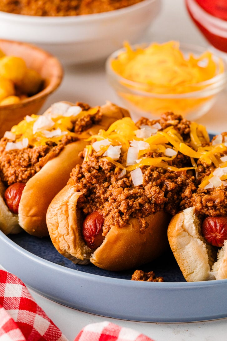 Chili cheese dogs on a blue plate with tater tots and shredded cheese in the background.
