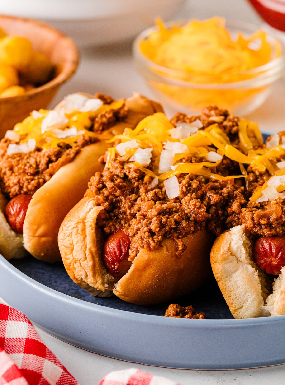 Chili cheese dogs on a blue plate with tater tots and shredded cheese in the background.