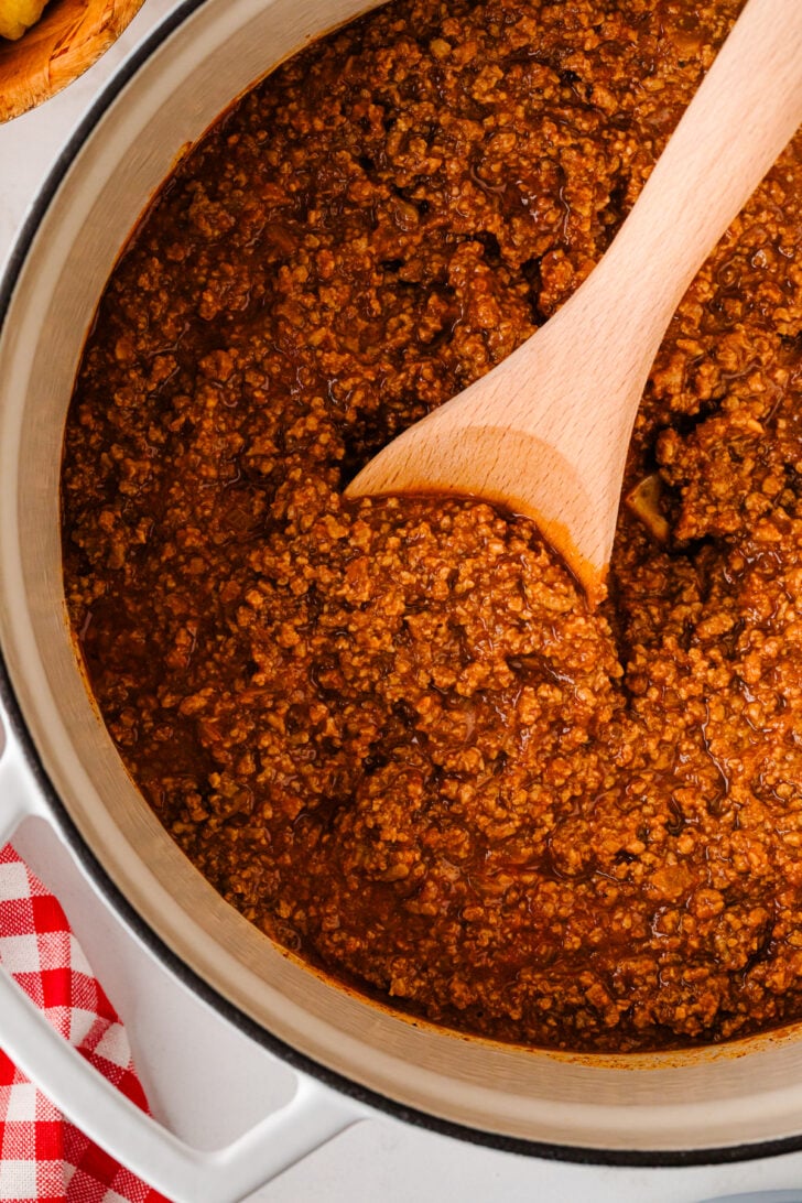 Homemade hot dog chili simmering in a pot with a wooden spoon.