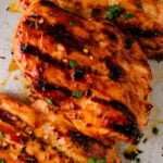 Close-up of grilled BBQ chicken breasts with char marks and fresh herbs.