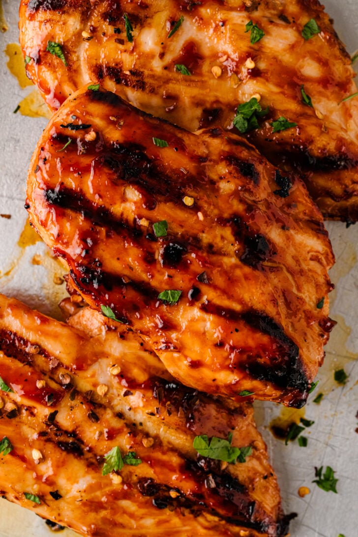 Close-up of grilled BBQ chicken breasts with char marks and fresh herbs.