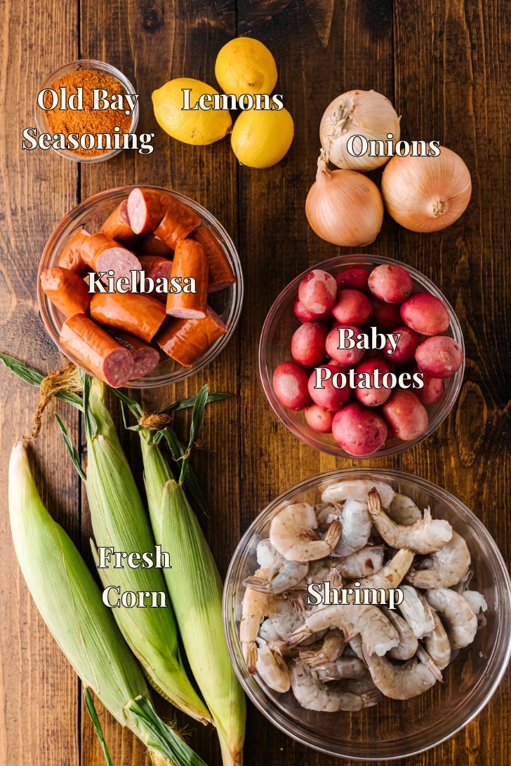 Labeled low country boil ingredients: Old Bay seasoning, lemons, onions, kielbasa, baby potatoes, corn, and shrimp.