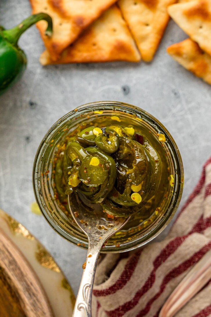 Cream cheese topped with candied jalapeño slices on a green plate with crackers and a jar of cowboy candy in the background.