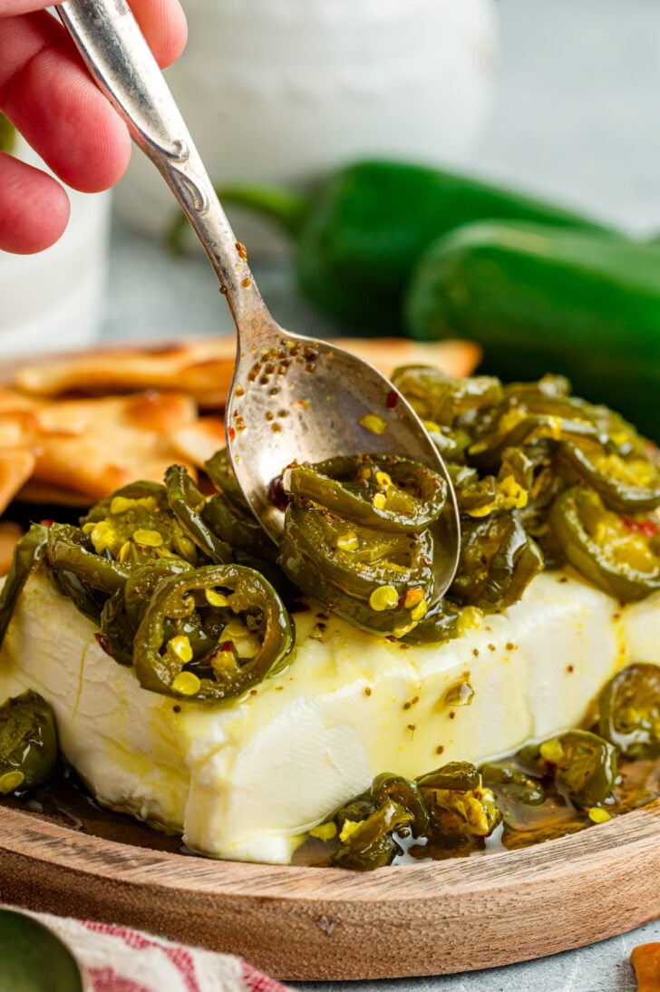 Candied jalapeños spooned over a block of cream cheese with crackers and a mason jar of cowboy candy in the background.