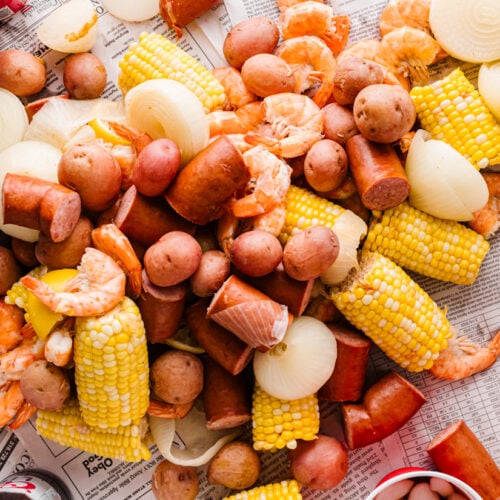 Wide shot of a low country boil spread on newspaper with shrimp, sausage, corn, potatoes, and dipping sauces.