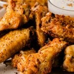 Close-up of crispy air fryer chicken wings with golden, seasoned skin on a plate with a red rim.